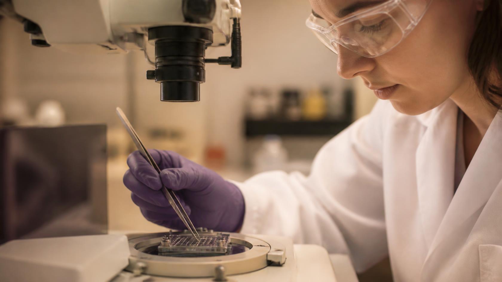 A researcher in safety glasses placing a sample under a microscope in a biosensing lab.